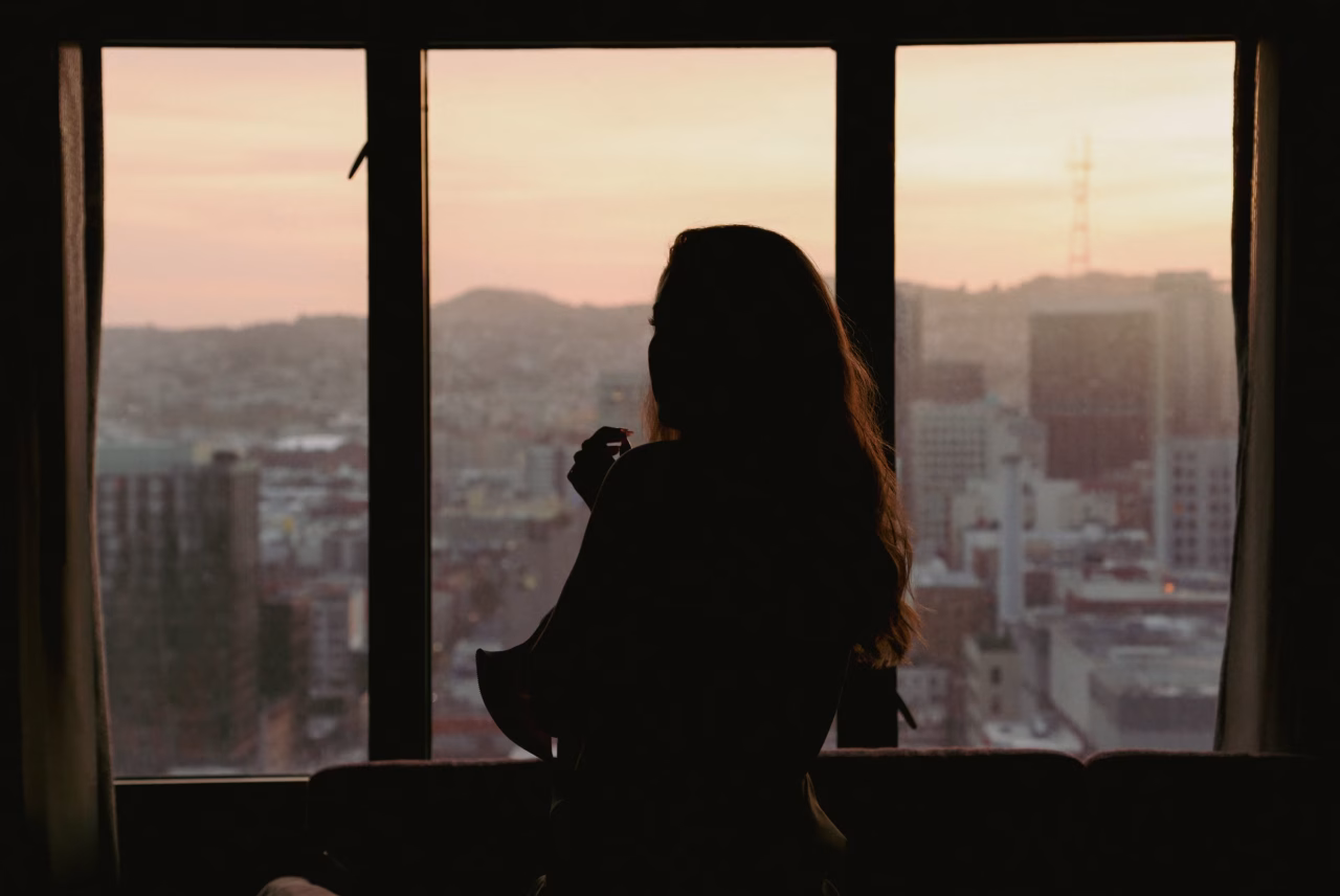Mujer mirando por la ventana, en Medellín, reflexionando sobre su experiencia como escort.